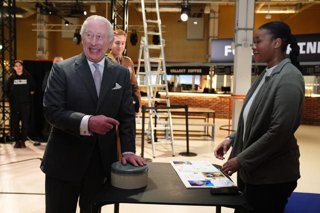Charles smiles as he is gifted some cake during his visit to Aviva Studios