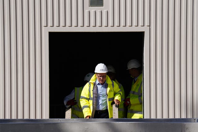 Sir Keir Starmer in a hard hat and yellow high-vis jacket framed by a grey metal doorway 