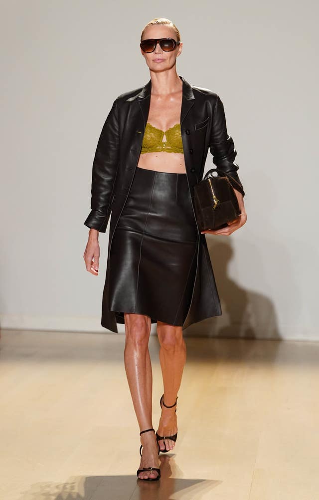 Jodie Kidd walking the catwalk in a green bralette with leather jacket and skirt, wearing aviator sunglasses 