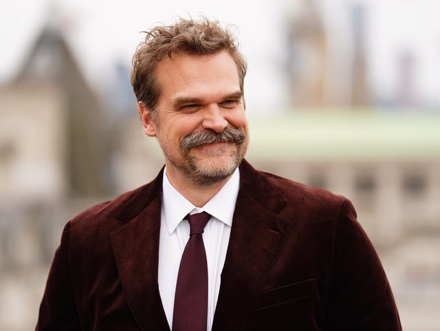 David Harbour in a red velvet suit and tie with moustache.