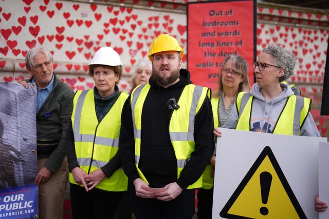 Campaigners in yellow hard hats and hi-viz vests in front of the Covid Memorial Wall