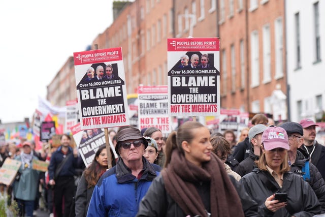People on a protest march holding posters which read 'Blame the Government, not the migrants'
