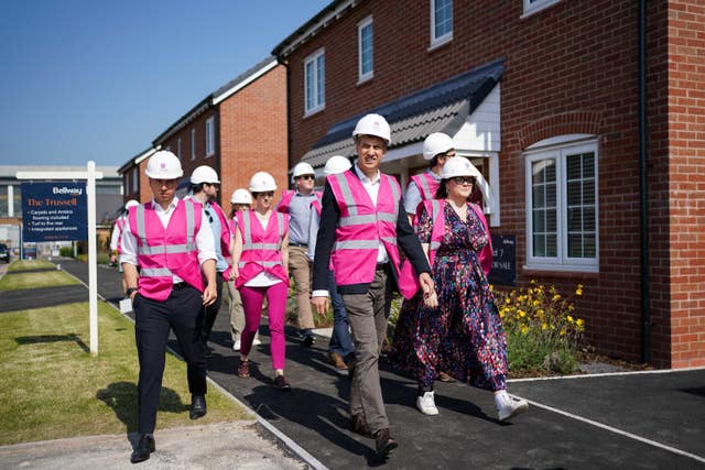 Ed Miliband walks past new-build homes wearing a hard hat and pink hi-vis with a group of people
