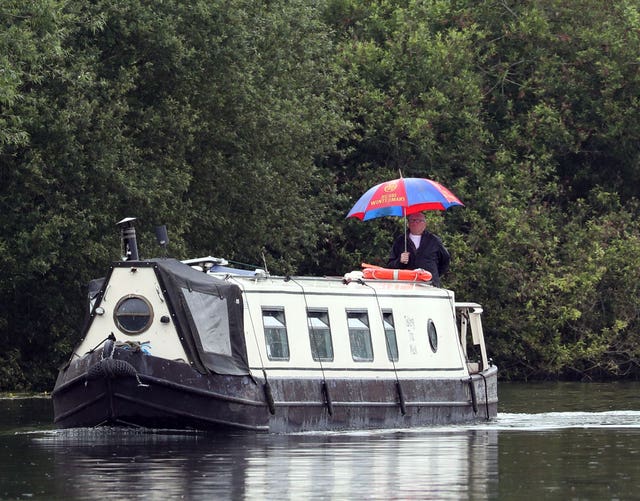 A man on a narrowboat uses an umbrella near Henley-on-Thames