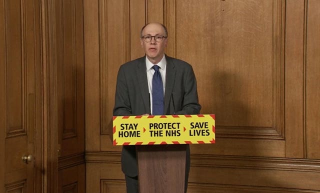 Professor Sir Stephen Powis speaking from a lectern, which has a yellow sign on it reading 'Stay home, Protect the NHS, Save lives'