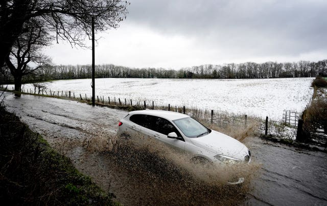 A car passes through floodwaters next to a snow-covered field near Wrotham in Kent