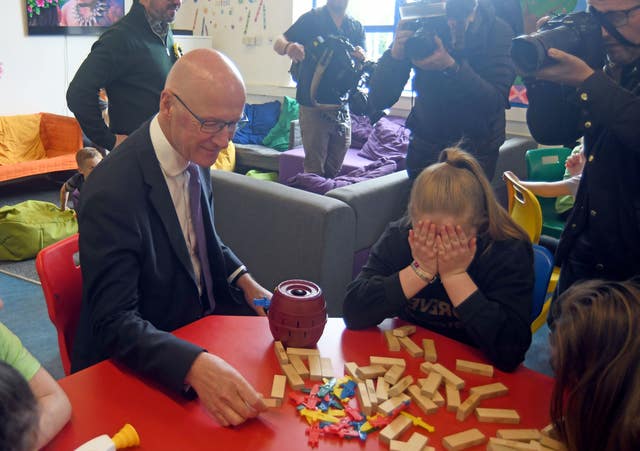Scottish First Minister and SNP leader John Swinney plays with Jenga blocks as a child hides her face behind her hands, during a visit to the Jeely Piece Club in Glasgow