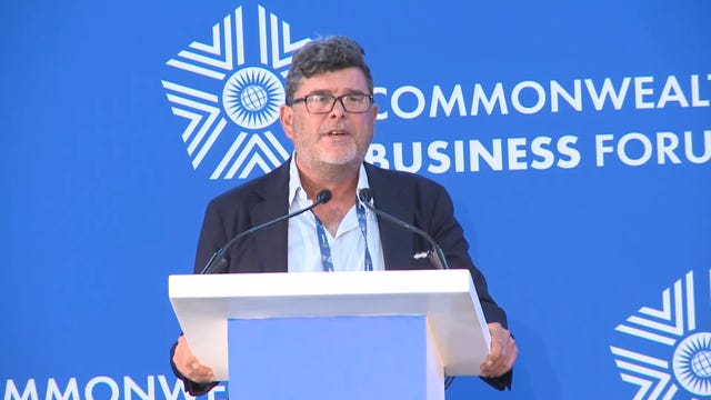 Frank Hester gives a speech during the Commonwealth Heads of Government Meeting in Rwanda. He stands at a lectern and in front of a blue background bearing the words Commonwealth Business Forum