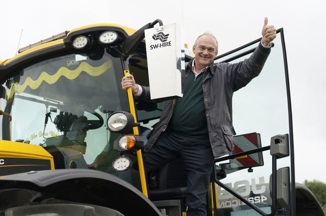 Sir Ed Davey gives a thumbs up gesture has he climbs out of a tractor