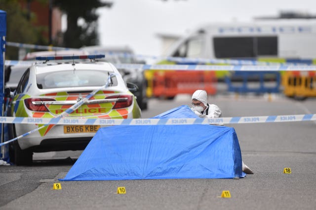 A police forensic officer looks under a small blue police tent covering an area of road in Irving Street in Birmingham (Jacob King/PA)