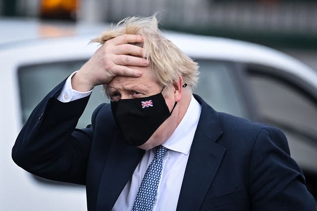Boris Johnson runs his hands through his hair while wearing a mask