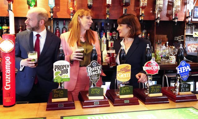 Labour frontbenchers Jonathan Reynolds, Angela Rayner and Rachel Reeves standing behind a row of beer pumps on a pub bar holding glasses of beer