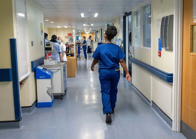 A nurse walks through a corridor in a hospital, with other staff in the distance