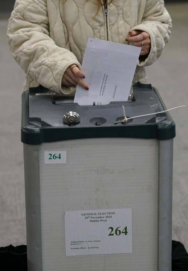 A woman in a white coat drops her vote into a ballot box