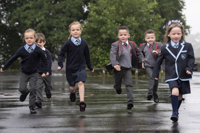 Six young schoolchildren dressed in their uniforms run across a playground in the rain