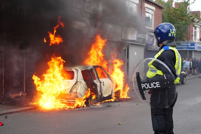 A police officer in riot gear looks on while a car burns on a street in Middlesbrough during an outbreak of far-right violence