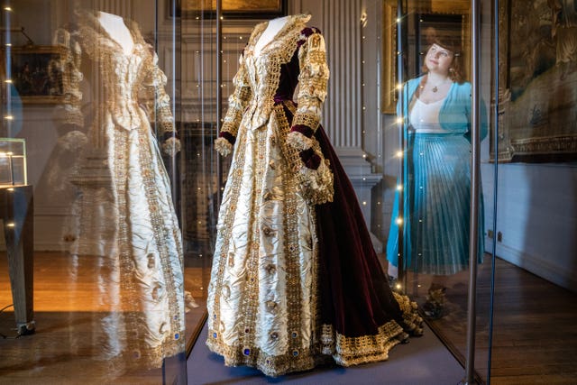 A Mary, Queen of Scots costume on display in a cabinet, with a woman looking at it
