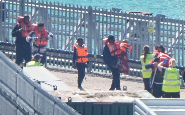 People wearing life jackets make their way towards people in hi-vis vests