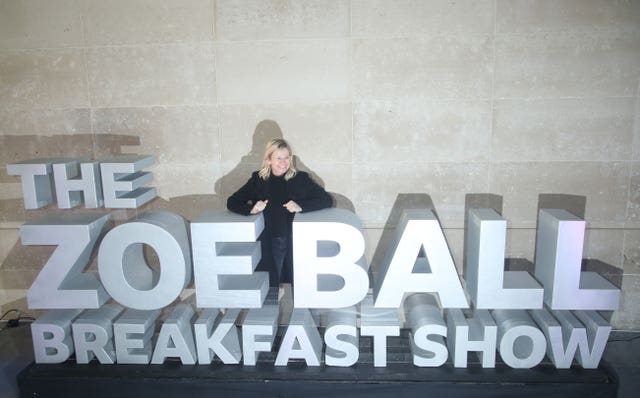 Zoe Ball next to a large sign reading The Zoe Ball Breakfast Show