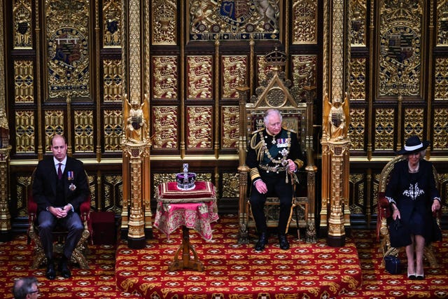 The Prince of Wales (centre) sits by the Imperial State Crown with the Duchess of Cornwall (right) and the Duke of Cambridge (left) during the State Opening of Parliament in the House of Lords, London