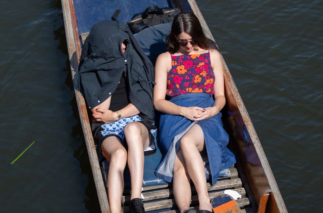A woman shelters under a coat during a punt ride 