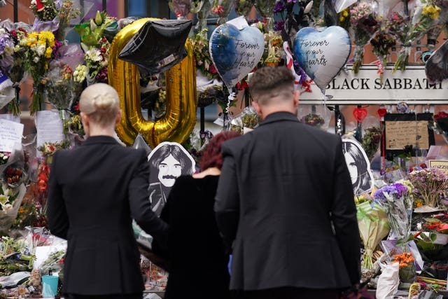 Kelly, Sharon and Jack Osbourne view the messages and floral tributes left at the Black Sabbath Bridge bench after the funeral procession in Birmingham