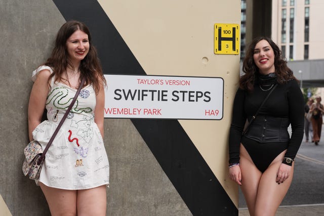 Two fans standing either side of a sign reading 'Taylor's Version, Swiftie Steps, Wembley Park, HA9'