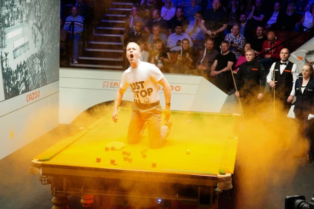 A Just Stop Oil protester jumps on the table and throws orange powder on during the match between Robert Milkins against Joe Perry at the Crucible