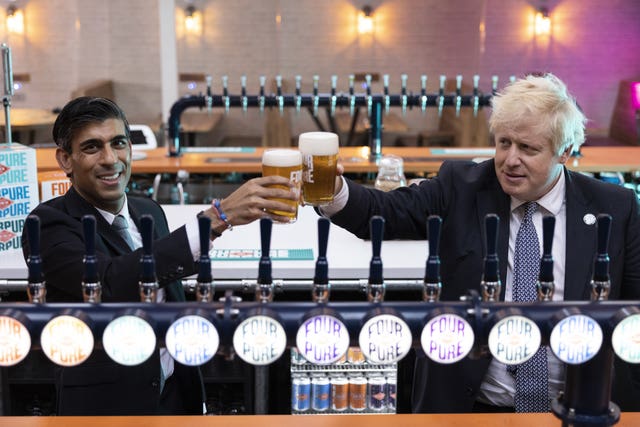 Boris Johnson and Rishi Sunak clinking pints of beer behind a bar