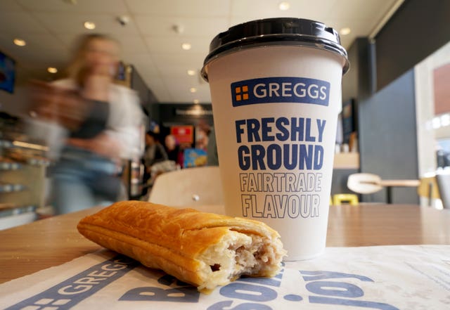 A sausage roll and a coffee sits on a table in a Greggs store