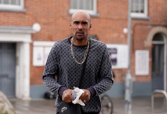 Ashley Warren, wearing large gold chains and holding a bottle of water, outside court