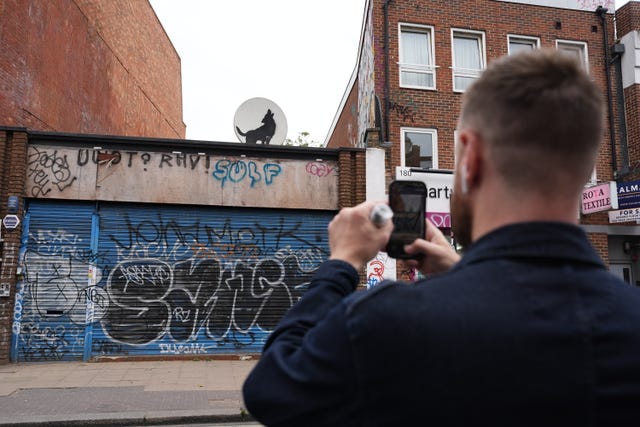 A man takes a picture of the new howling wolf Banksy in Peckham, south London