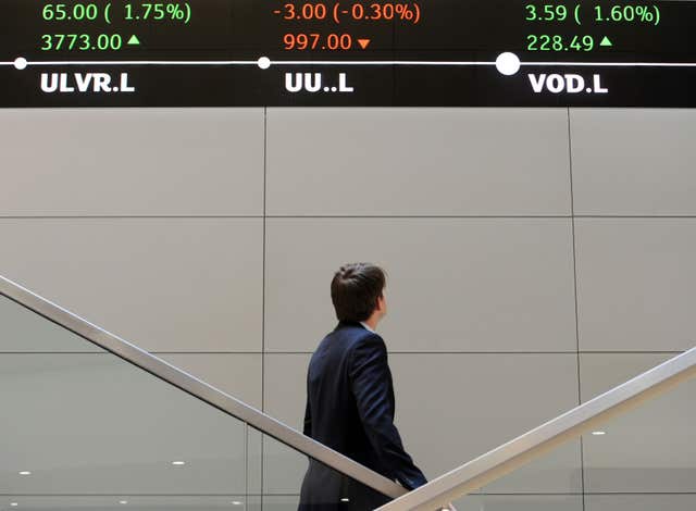 A man looks up at electronic ticker tape showing the FTSE 100 inside the London Stock Exchange