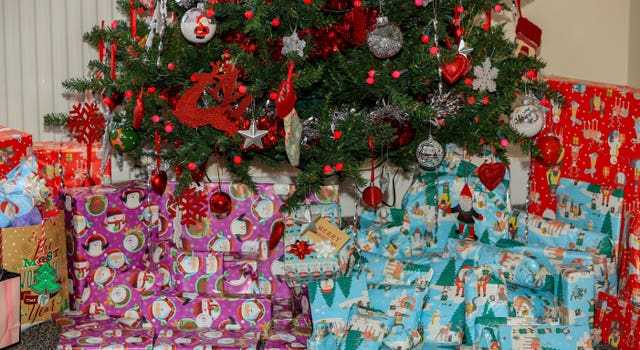 A pile of neatly wrapped Christmas presents beneath a Christmas tree (Peter Byrne/PA)