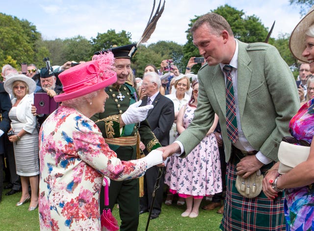 The late Queen shakes hands with Doddie Weir, with a crowd of onlookers behind them