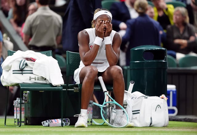 Coco Gauff sitting with her head in her hands by the side of a tennis court 