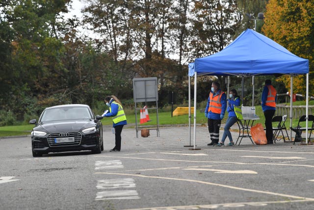 A tester is watched by her colleagues as she talks to the occupants of a car at a mobile coronavirus testing centre which has been set up at Stratford Park Leisure Centre in Stroud, Gloucestershire (Ben Birchall/PA