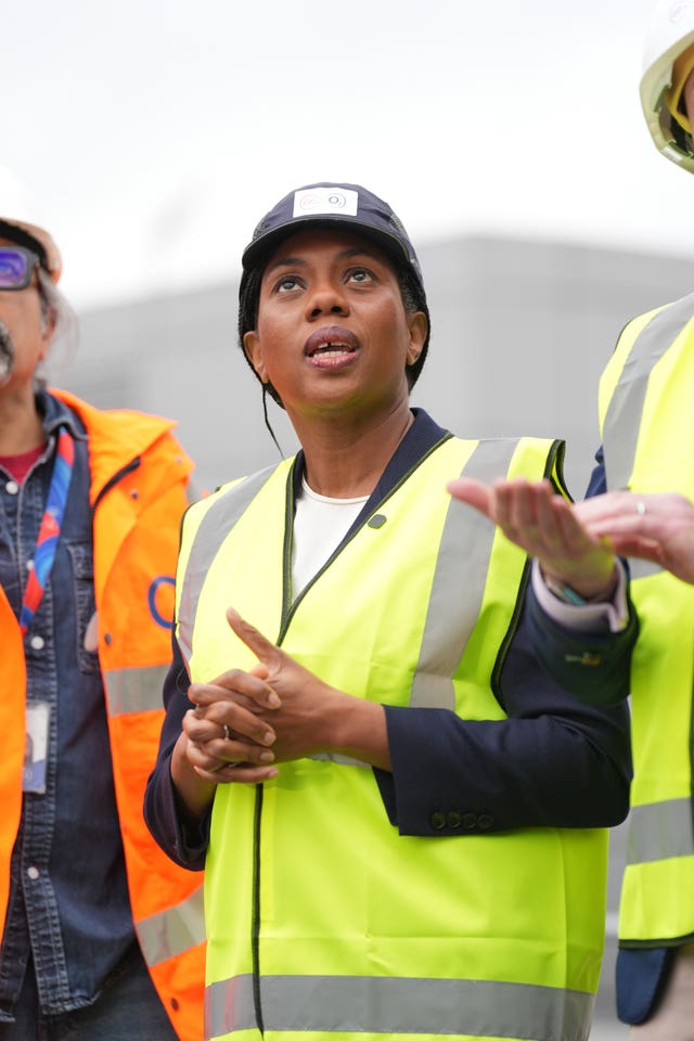 Kemi Badenoch in high vis jacket and hard hat looking up at something out of shot