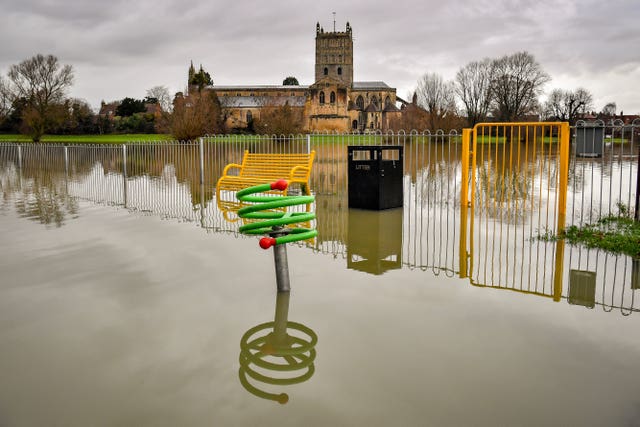 Children’s playground equipment pokes out from floodwater surrounding Tewkesbury Abbey (Ben Birchall/PA)