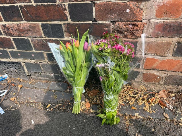Two bunches of flowers are set against a red brick wall, they are still in the plastic but the buds are opening to show pink and orange flowers