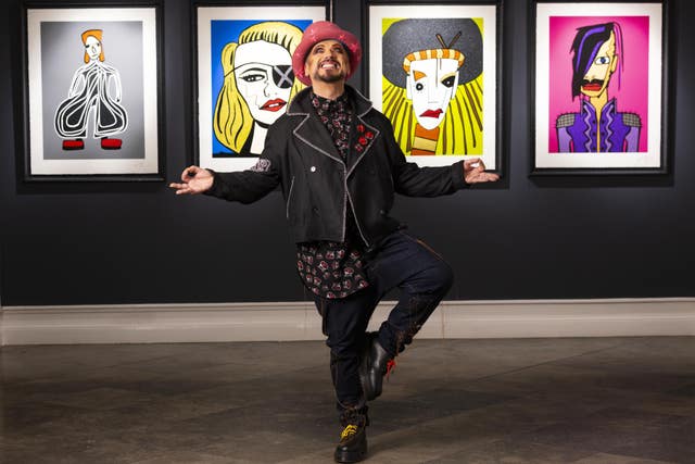 Boy George standing on one leg in front of his portraits