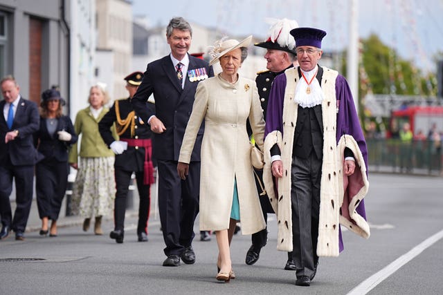 Princess Royal walking alongside dignitaries, with her husband behind her