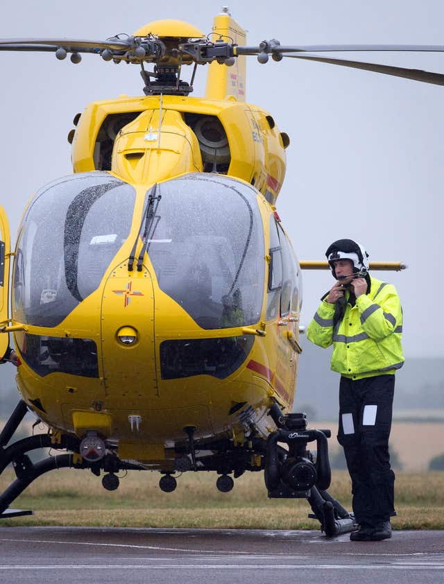 William putting a helmet on as he stands next to an East Anglian Air Ambulance helicopter 