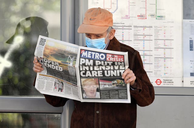 A man wearing a facemask at a bus stop reading a newspaper outside St Thomas’ Hospital in Central London where Prime Minister Boris Johnson was in intensive care
