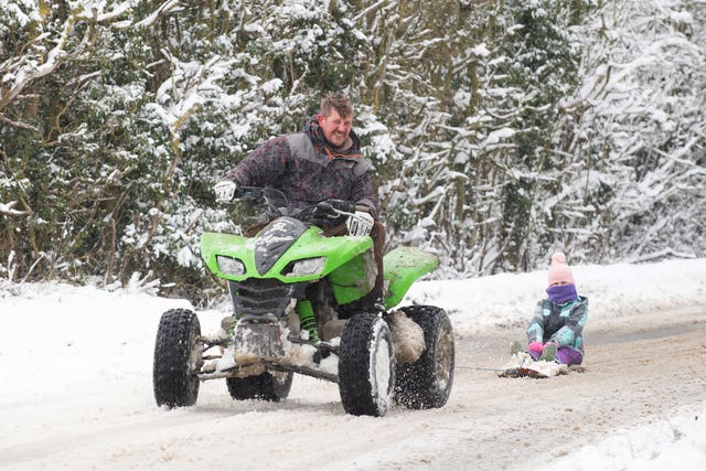 Richard Squirrell uses a quad bike to give his granddaughter Florence a ride in the snow in Wattisham in Suffolk 