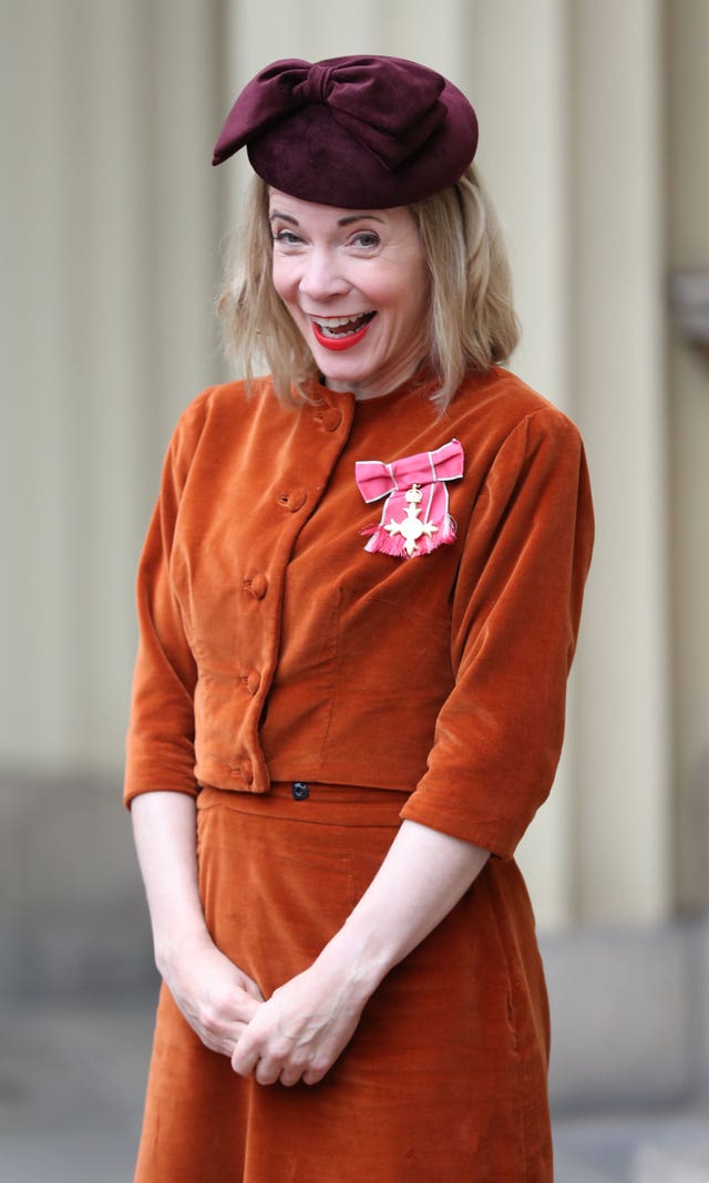 Lucy Worsley wearing an orange suit and purple beret, with her hands clasped together.