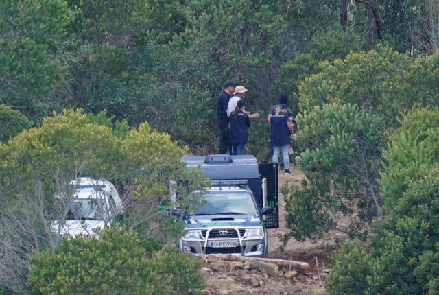 Official vehicles parked on wooded land near the reservoir, with members of the search team standing nearby.