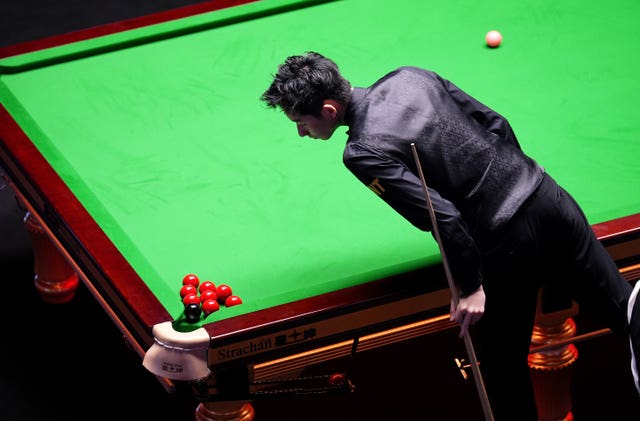 Wu Yize observes a cluster of reds and the black over the pocket during the 14th frame against Mark Allen