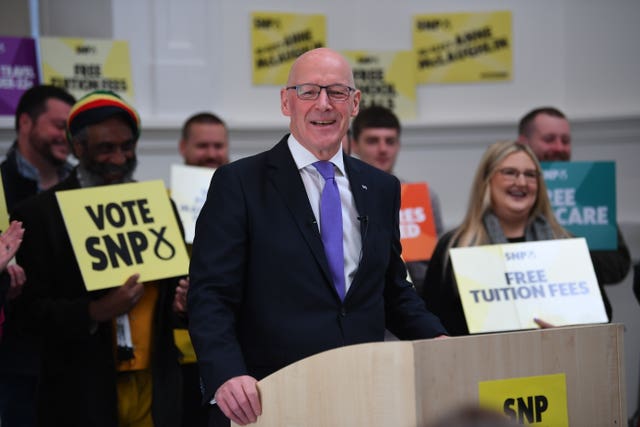 John Swinney at lectern, with SNP supporters behind him