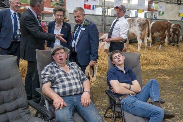 A couple of farmers sleep as the Princess Royal tours the cattle stalls in the Highland Hall during a visit to the Royal Highland Show at the Royal Highland Centre in Ingliston, Edinburgh